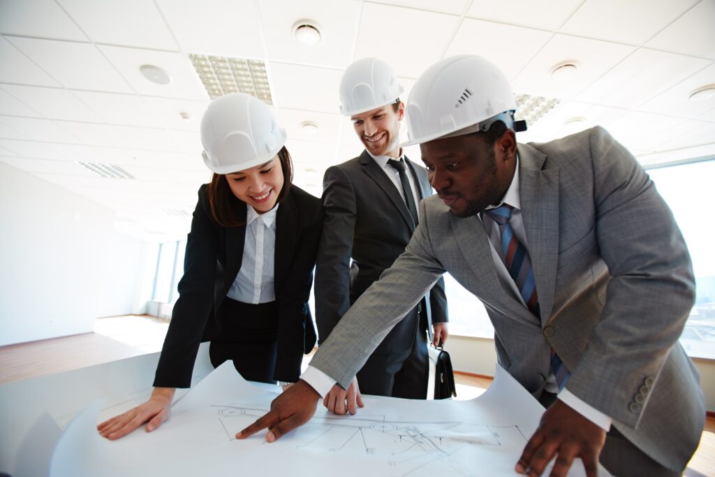 Group of professional architects and engineers reviewing blueprints in a modern office, discussing kitchen and bathroom renovation plans in London.
