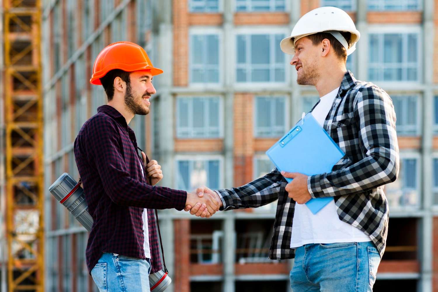 Two construction professionals wearing hard hats shaking hands at a building site, representing a contactor in London.