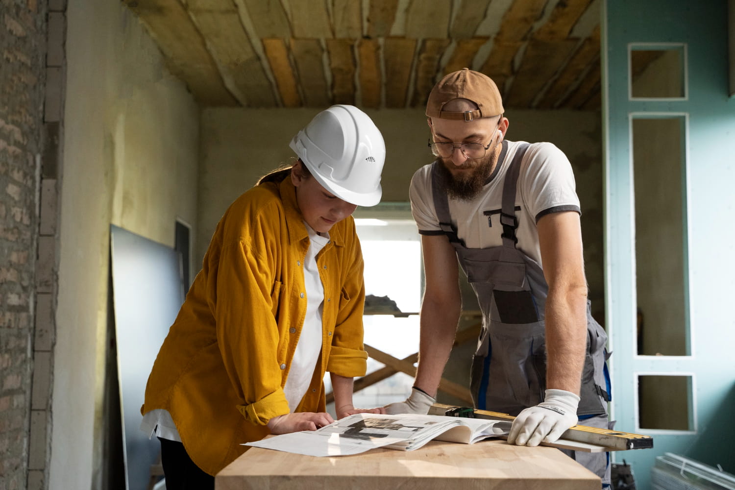 Two professional builders reviewing construction plans during a home renovation in London interior with exposed brick and wooden ceiling
